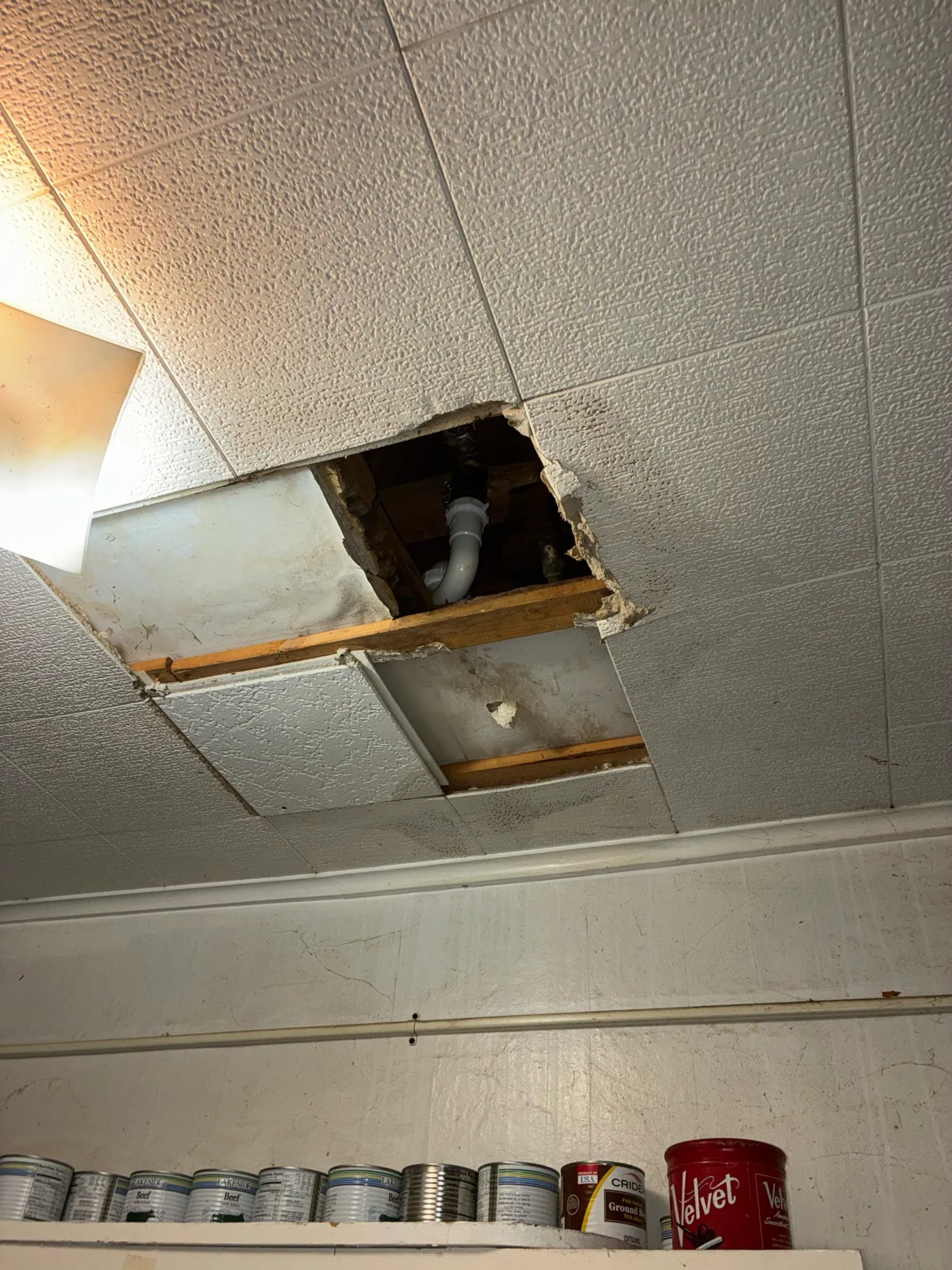 A drop ceiling opened up to reach the drain line above